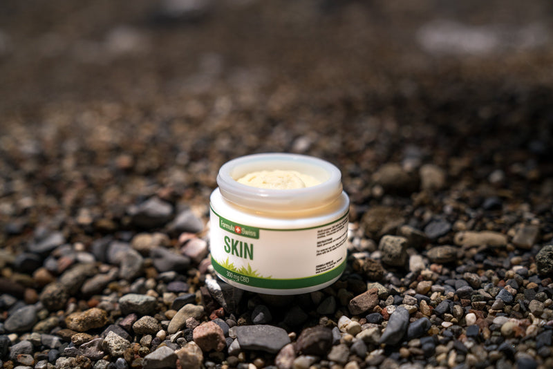 Frasco aberto de bálsamo CBD Skin da Formula Swiss, 300 mg de CBD, numa praia de seixos