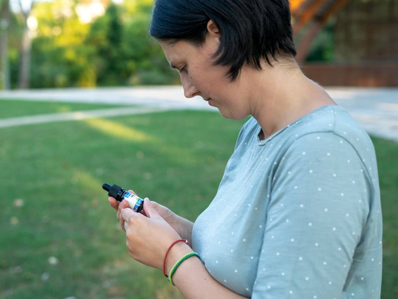 Mulher ao ar livre a olhar para um frasco de óleo de CBD da Formula Swiss na mão