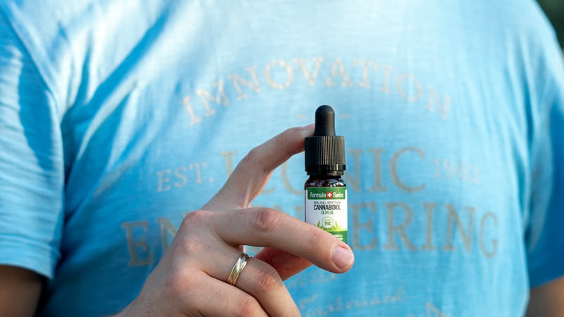 A hand holding a 10 ml bottle of Formula Swiss CBD oil in olive oil